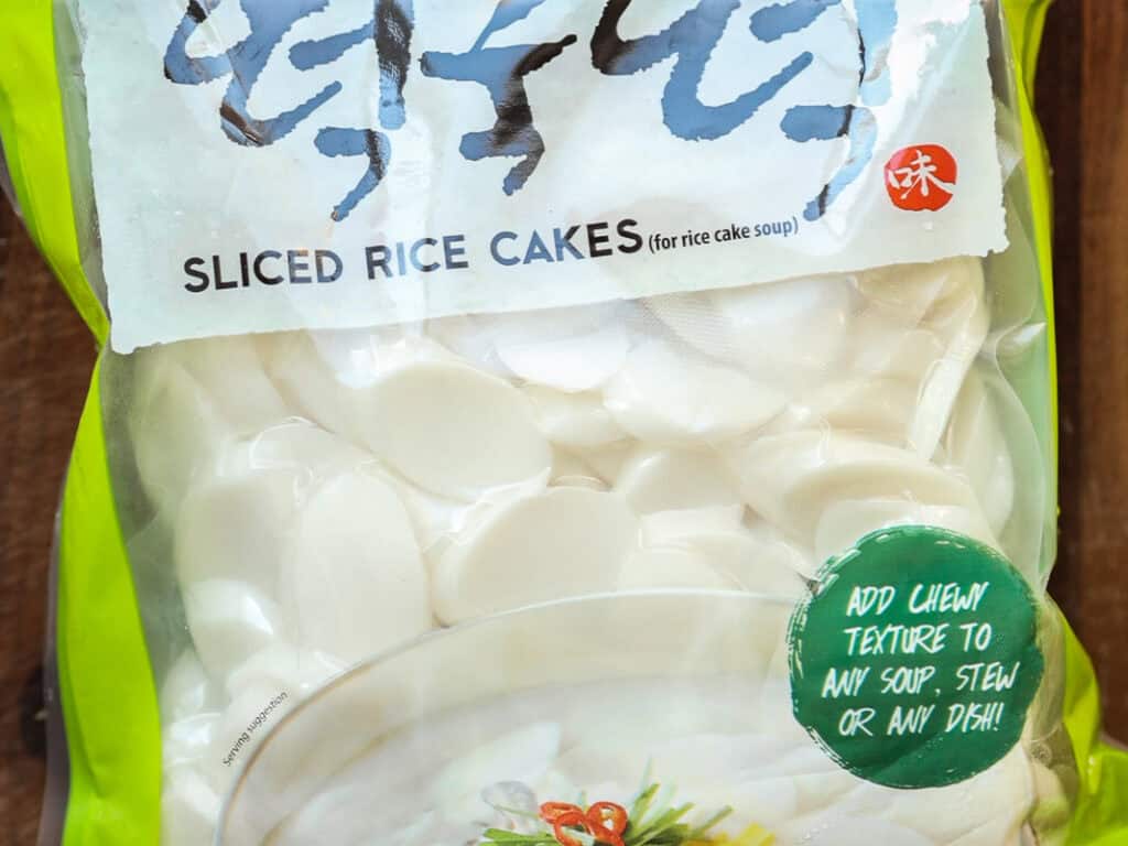 A package of sliced rice cakes for soup, with clear plastic showing white oval slices inside. The green and red label suggests adding them to soups or stews for a chewy texture. The top of the package has stylized text.